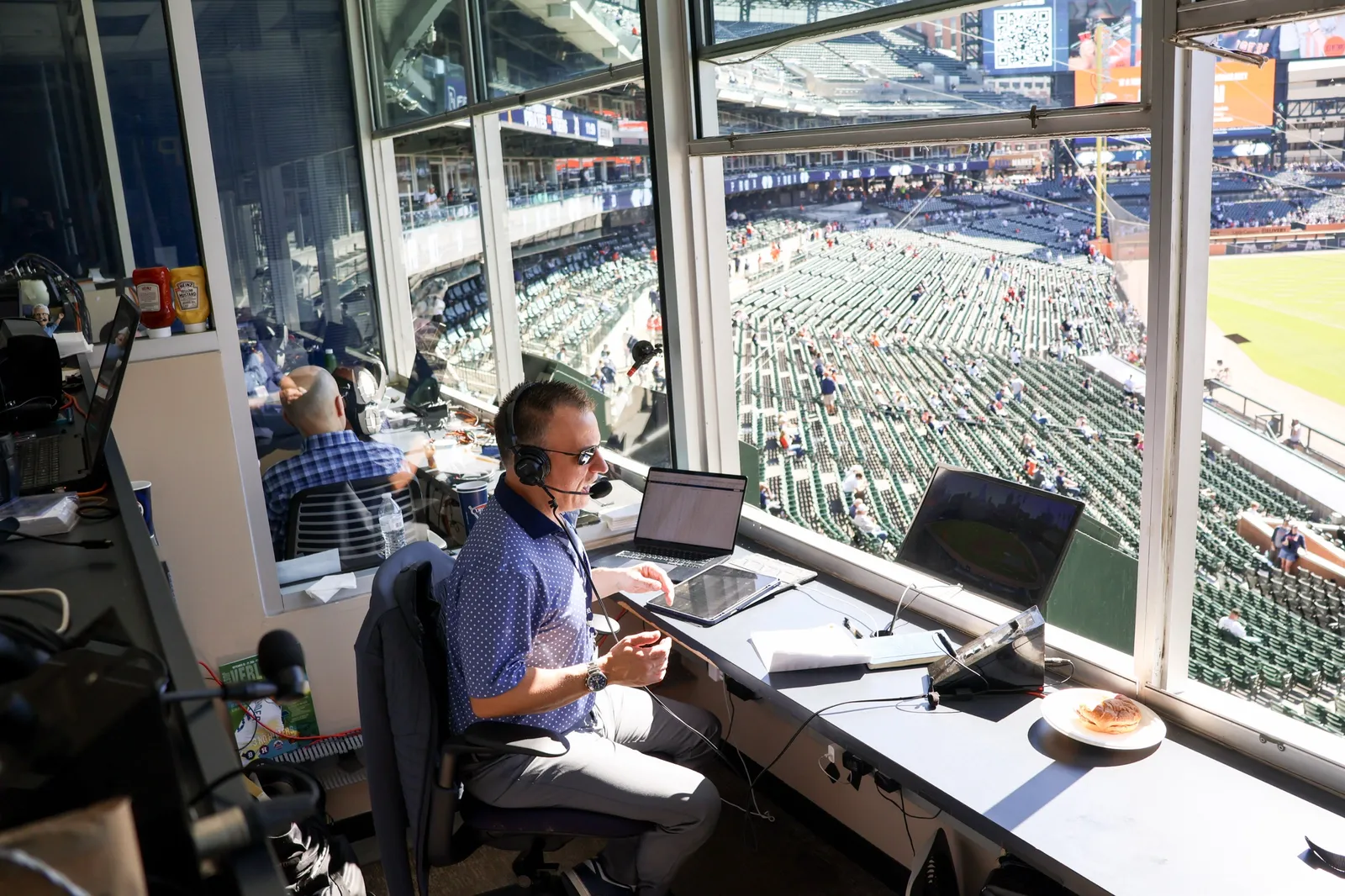 Greg Gania on the air in the Comerica Park radio booth, with the stands and field below