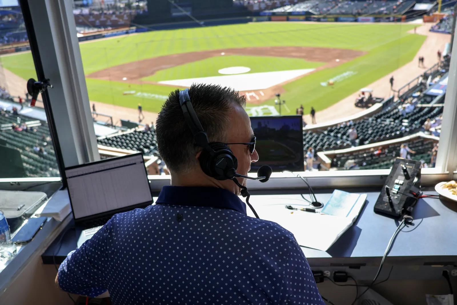 Greg Gania in a headset calling a game from the radio booth above the field at Comerica Park