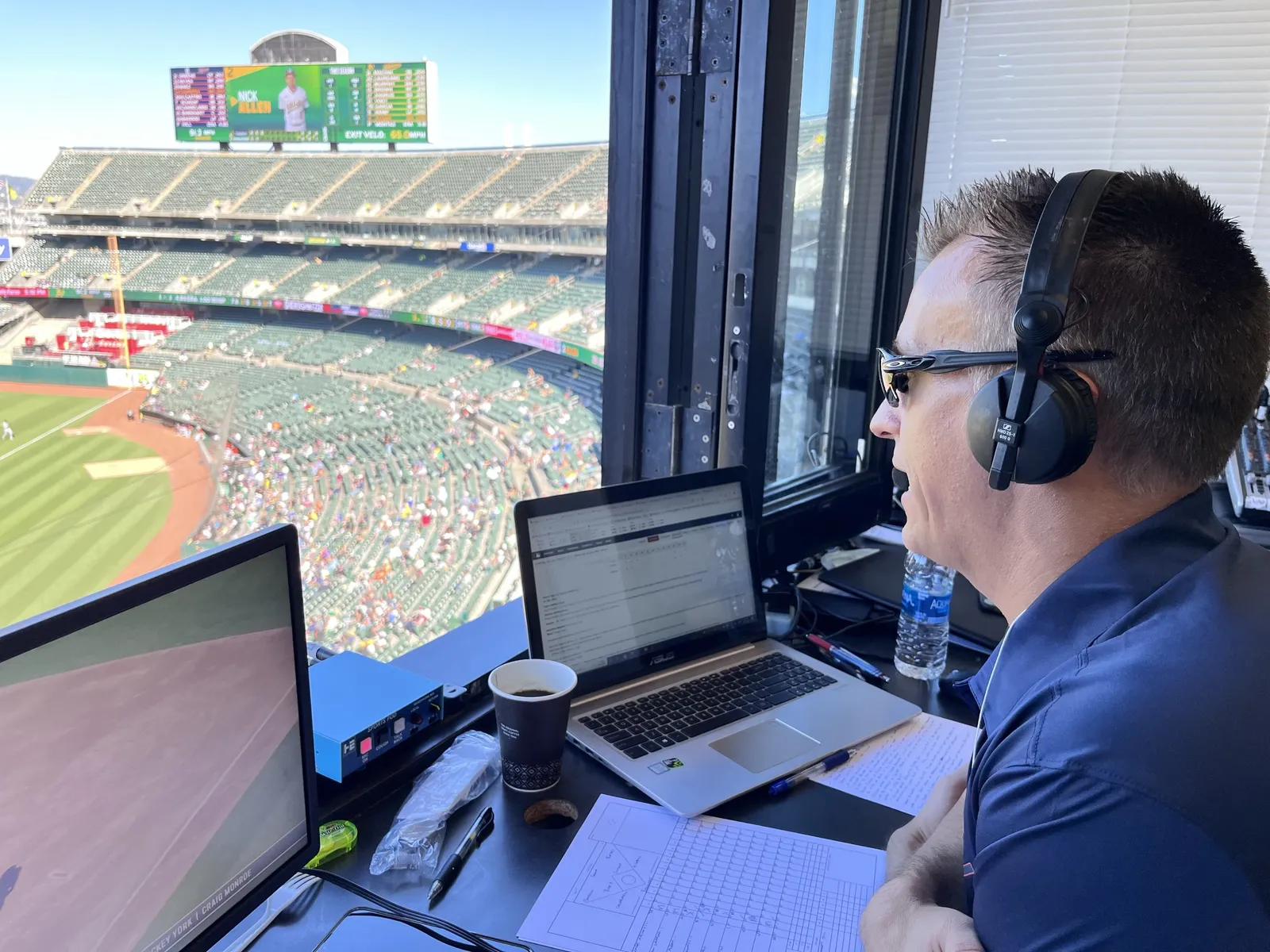 Greg Gania calling a game in headphones from the visiting radio booth overlooking the field in Oakland